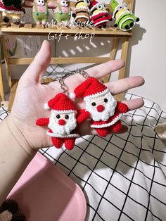 the hand is holding two small crocheted santa clauses on it's fingers