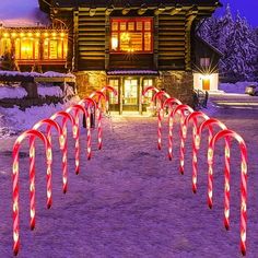 lighted candy canes are in front of a log cabin at night with snow on the ground