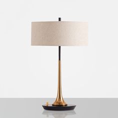 a table lamp with a white shade on it and a black plate underneath the lamp