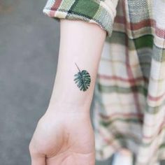 a person with a small green leaf tattoo on their left wrist and the other arm