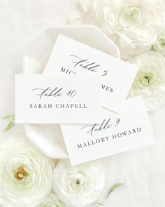 wedding place cards with white flowers and greenery on a tableclothed cloth background