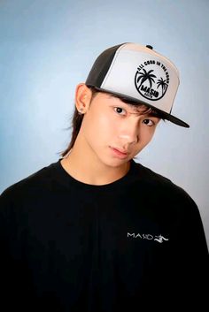 a young man wearing a black and white hat with palm trees on the front, against a blue background