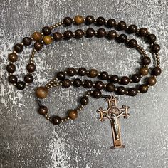 Exquisite Catholic Rosary featuring black wooden beads and a bronze-tone crucifix, Wood Bead rosary, Catholic Gifts, Cord Rosary Immerse yourself in the craftsmanship of this intricately fashioned Catholic rosary, distinguished by its remarkable elegance and unique nature. Formed from 10mm beads of green cypress wood, this rosary truly encapsulates devotion. Enhanced by a 2.4-inch crucifix, the beads are expertly threaded and carefully knotted onto micro cord, ensuring both lasting durability an 8mm Bead Crucifix Rosary For Meditation, Crucifix Rosary With 8mm Beads For Meditation, 108 Beads Cross Rosary For Meditation, Spiritual Rosary With 108 Beads And Crucifix, Brown Cross-shaped Rosary With Wooden Beads, Brown Beaded Rosary With Cross Shape, Meditation Rosary With Wooden Beads And Cross Shape, Brown Cross Rosary In Spiritual Style, Brown Wooden Beaded Cross Rosary