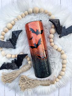 an orange and black glitter tumbler with bats on it next to wooden bead garland