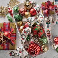 assorted christmas ornaments and decorations on a platter next to wrapping paper, ribbons and bows