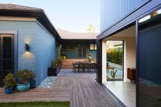 an outdoor patio with wooden decking next to a blue house and dining room area