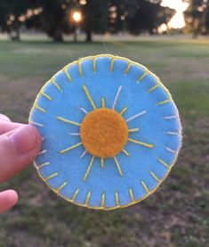 a hand holding up a small blue and yellow sunflower broochie in the middle of a field