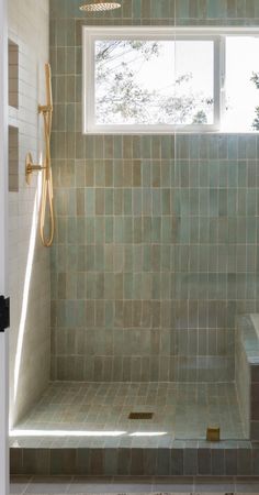 a bathroom with green tiles and a window in the shower area, along with a bench