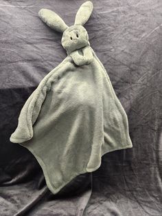 a stuffed animal laying on top of a bed covered in a gray blanket and covering it's head