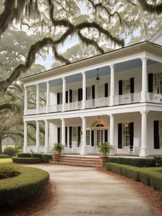 a large white house with black shutters on the front and porches, surrounded by trees