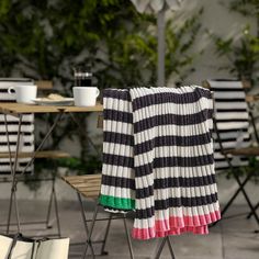 a striped blanket sitting on top of a chair next to a table with cups and plates