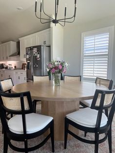 a dining room table with four chairs and a vase of flowers on the table in front of it