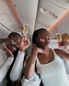 two women holding champagne flutes in their hands while sitting on an airplane with the seats down