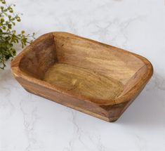 a wooden bowl sitting on top of a white counter next to a potted plant