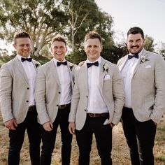 a group of men standing next to each other wearing suits and bow ties with trees in the background