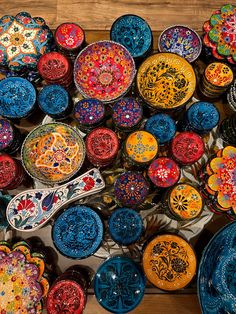 many different colored plates and bowls on a wooden table with one sitting in the middle