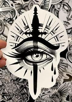 someone holding up a sticker with an all seeing eye in the center and a knife sticking out of it