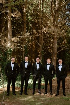 a group of men in tuxedos standing next to each other near some trees