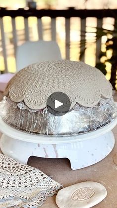 a cake sitting on top of a white plate covered in tin foil and surrounded by doily