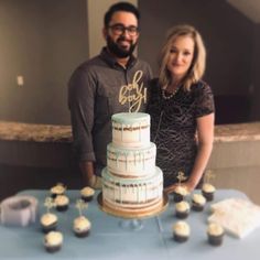 a man and woman standing next to a table with cupcakes in front of them