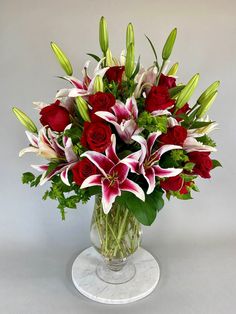 a vase filled with red roses and lilies on top of a white marble pedestal