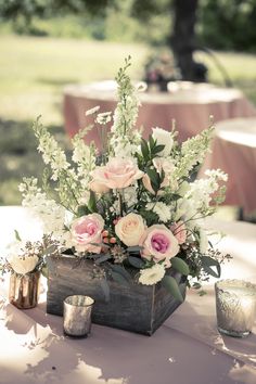 a wooden box filled with lots of flowers on top of a table next to candles