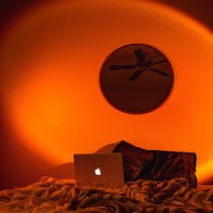 an apple laptop computer sitting on top of a bed under a round wall mounted clock