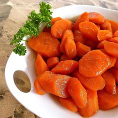 there is a white bowl filled with carrots and parsley on the beach side