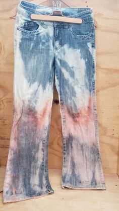 a pair of blue and pink tie dye jeans hanging on a wooden hanger in front of a wood wall