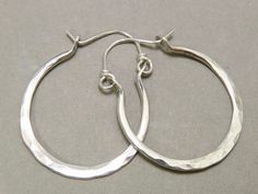 "Classic hammered hoops are made from medium 12 gauge sterling silver wire so they're not too heavy,  and have a full, round shape. Hammering \"spring hardens\" the metal so they snap back into position and will keep their shape over time.  They measure 1 5/8 inches long by 1 1/4 inches in width.  Curved wire closure slips through the back loop of the earring for a secure fit.  Polished to a high shine, these are a staple to any wardrobe.  Hammer marks appear on one side only, and the back side Artisan Small Hoop Sterling Silver Jewelry, Artisan Silver Round Hoop Earrings, Adjustable Nickel-free Sterling Silver Hoop Earrings, Adjustable Soldered Hoop Earrings For Gifts, Artisan Small Hoop Sterling Silver Earrings, Artisan Silver Nickel-free Hoop Earrings, Artisan Sterling Silver Hoop Earrings, Hand Forged Sterling Silver Round Hoop Earrings, Artisan Hammered Hoop Jewelry