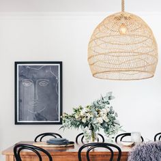 a dining room table with black chairs and a wicker light fixture