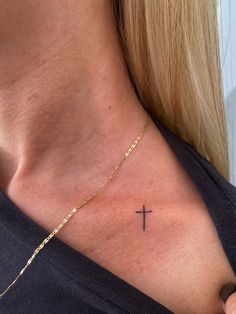 a woman with a cross tattoo on her chest is wearing a black shirt and gold necklace