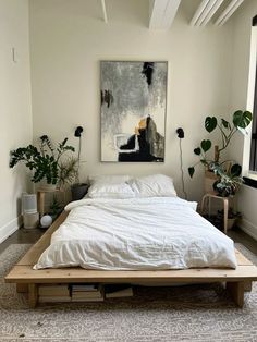 a white bed sitting in a bedroom next to a painting on the wall and potted plants