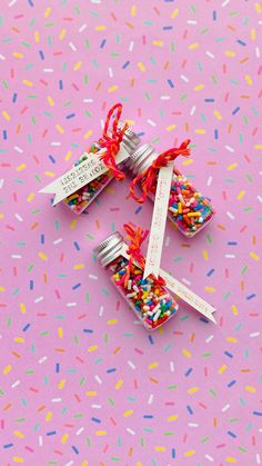 three small jars filled with sprinkles on top of a pink surface