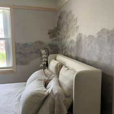 a white bed sitting under a window next to a wall with trees painted on it