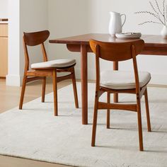 two wooden chairs sitting at a table with a white rug on the floor in front of it