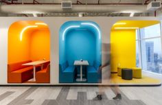 an office with colorful booths and tables in the center, while people walk past them