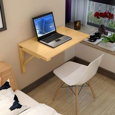 a laptop computer sitting on top of a wooden desk next to a white chair and window