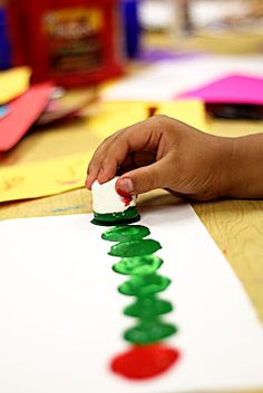 a child's hand is making a christmas tree out of construction paper