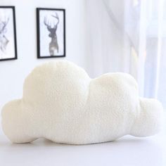 a white cloud pillow sitting on top of a table next to two framed pictures and a window