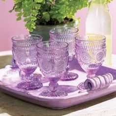 purple glassware is sitting on a tray next to a plant