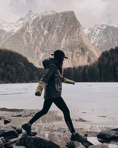 a woman walking on rocks near water with mountains in the background