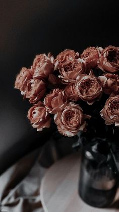 a black vase filled with pink roses on top of a table