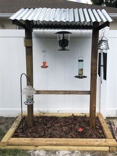 a bird feeder in the middle of a garden with birds hanging from it's roof