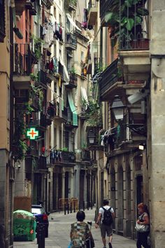 two people walking down an alley way with buildings on both sides and balconies above them