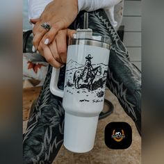 a person sitting on the ground holding onto a coffee cup with a cowboy drawing on it