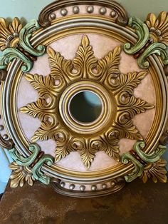 an ornate gold and white circular mirror on top of a wooden table next to a blue wall