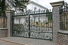 an iron gate and brick wall in front of a white building with a clock on it