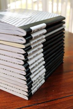 a stack of black and white books sitting on top of a wooden table next to a window