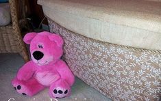 a pink teddy bear sitting on the floor next to a footstool in a living room